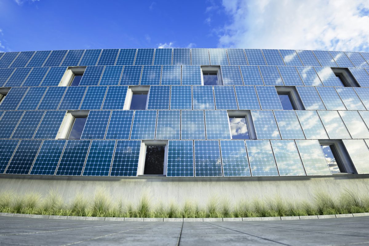 Modern building facade covered in solar panels, capturing renewable energy on a sunny day. Reflective glass windows integrated with clean energy technology, illustrating sustainable architecture.